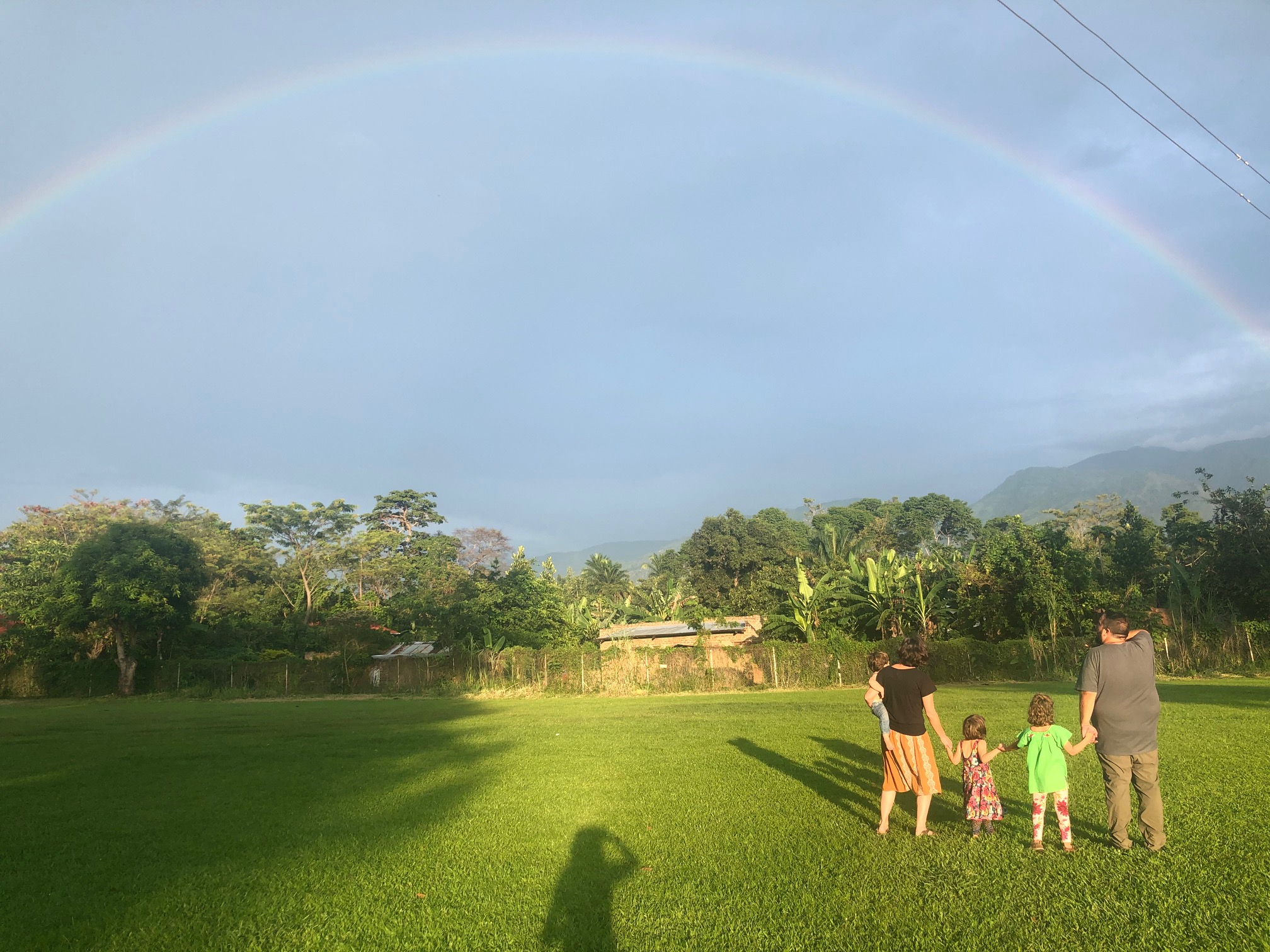 Family in a field viewing a rainbow.